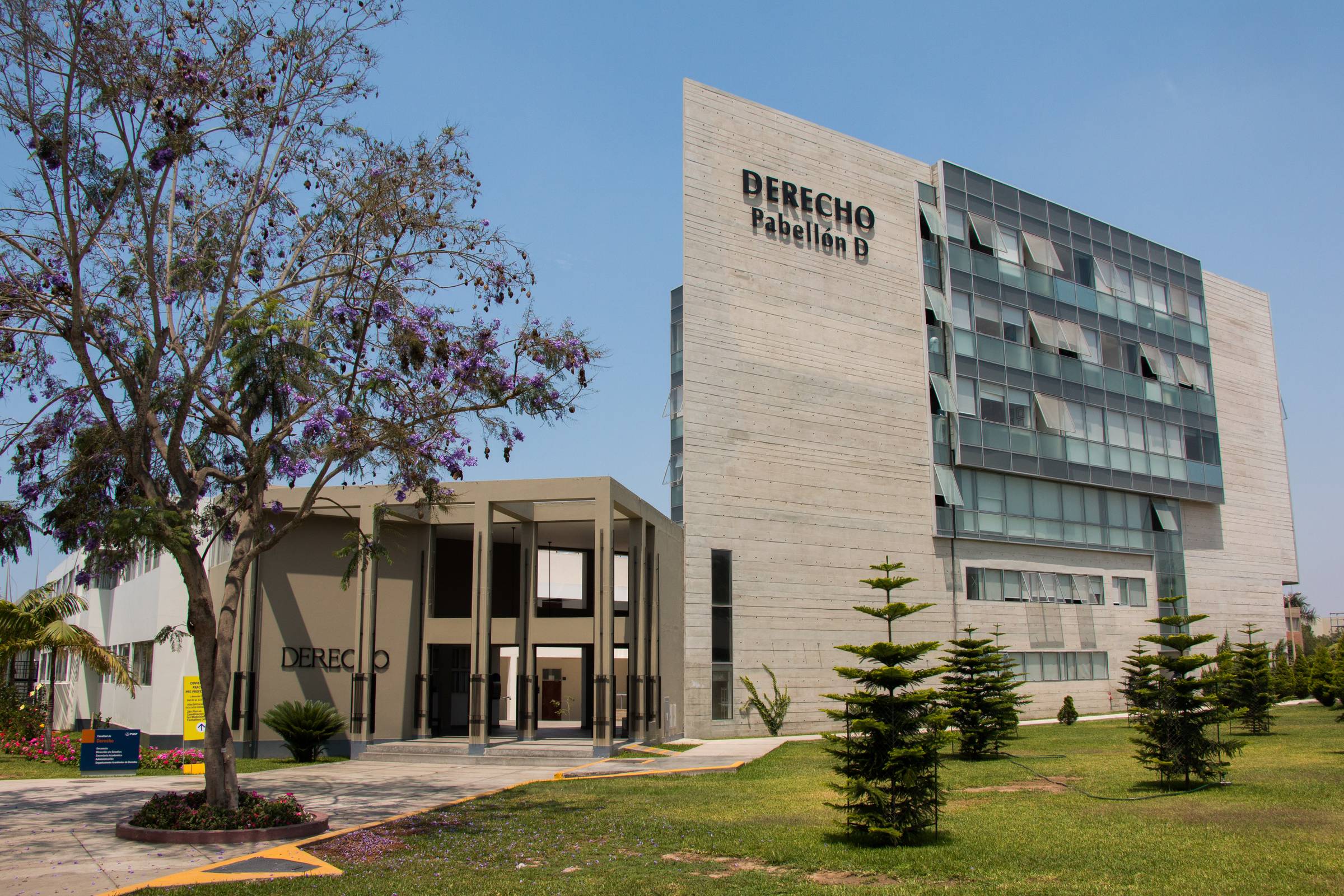 Vista exterior de la torre del edificio 'Derecho Pabellón D' con jardines y cielo despejado.